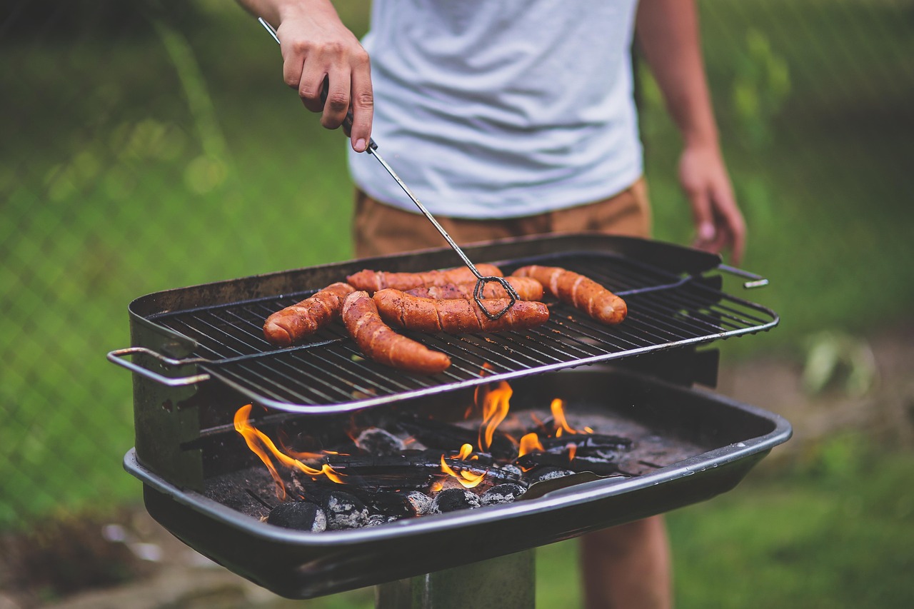 Bild eines Mannes, der auf einem Grill Würstchen zubereitet.